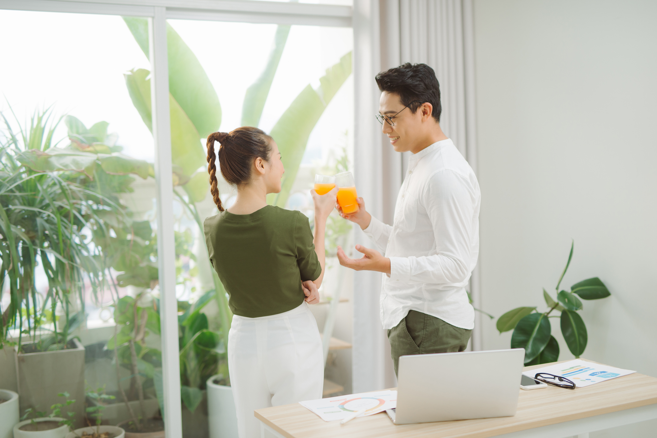 Adorable smiling couple bonding while working and drinking orange juice in bright warm sunny day